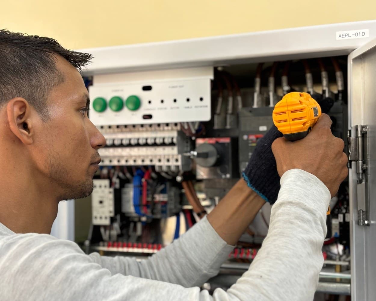 Un électricien casqué câble une armoire électrique