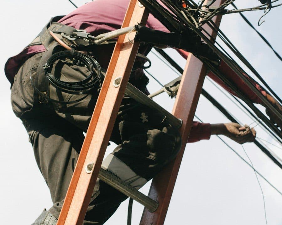 Un technicien sur une échelle travaille dans les câbles aériens