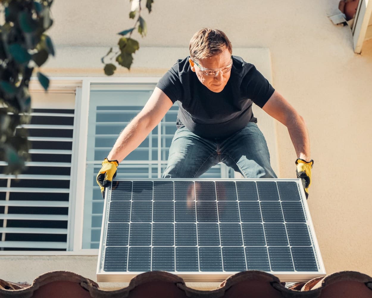 Un installateur porte un panneau solaire sur un toit