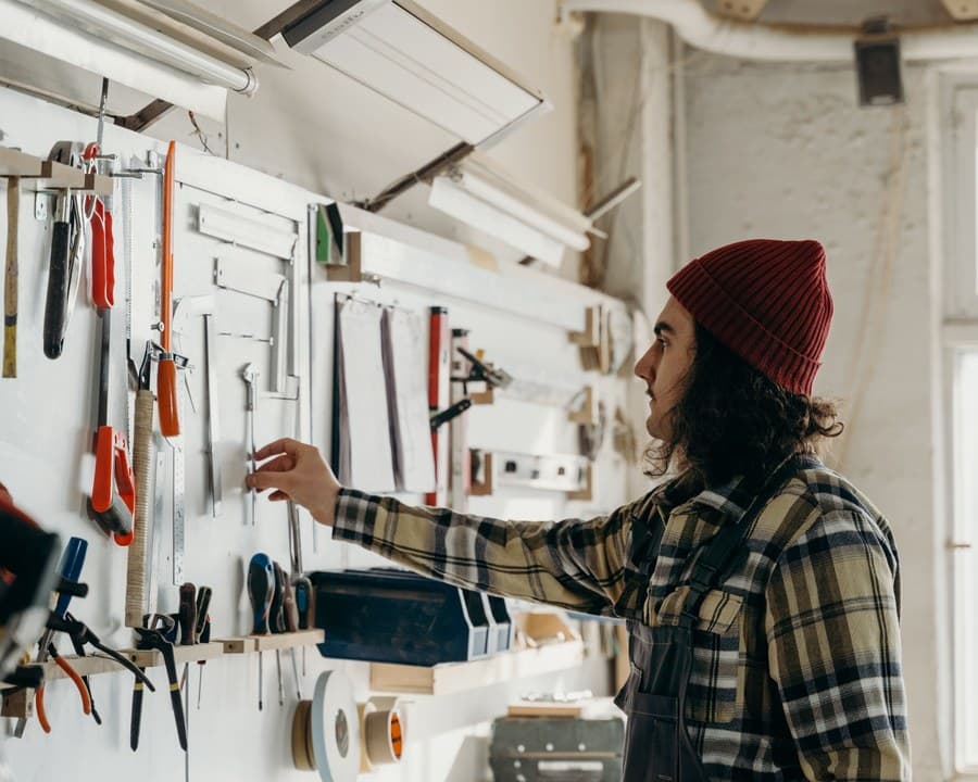 Un artisan choisit un outil au mur de son atelier