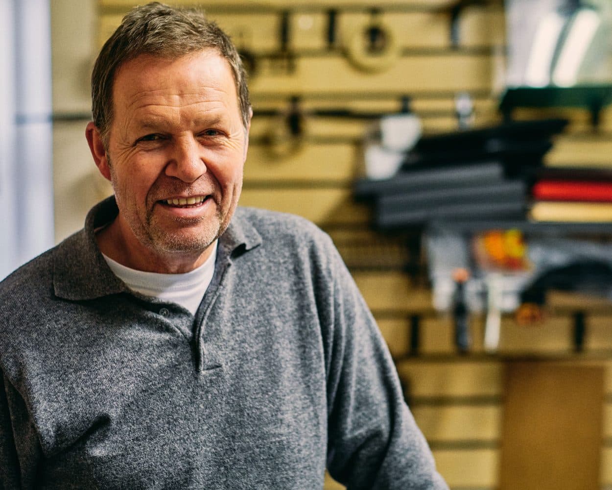 Un artisan sourit dans son atelier, outils accrochés au mur
