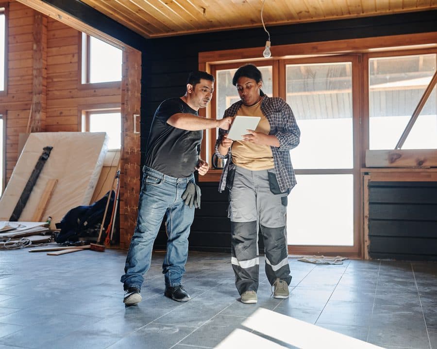 Deux artisans vérifient les plans sur tablette, maison en chantier