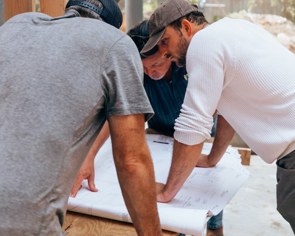 Trois artisans penchés sur les plans d’un chantier