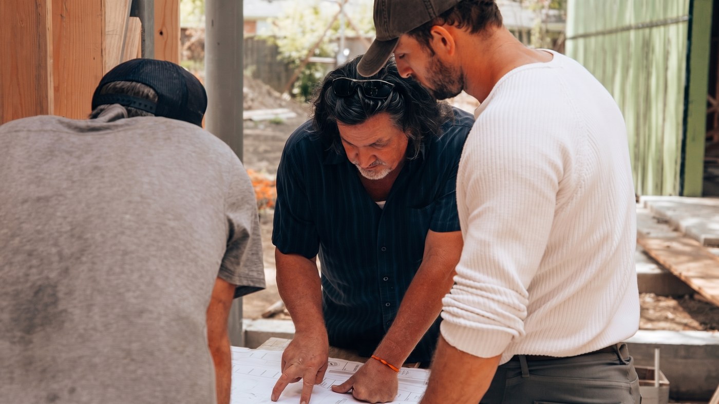Trois hommes lisent les plans sur un chantier de maison
