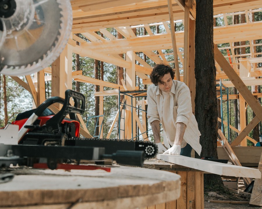 Deux artisans débitent une pièce de bois dans une maison en construction