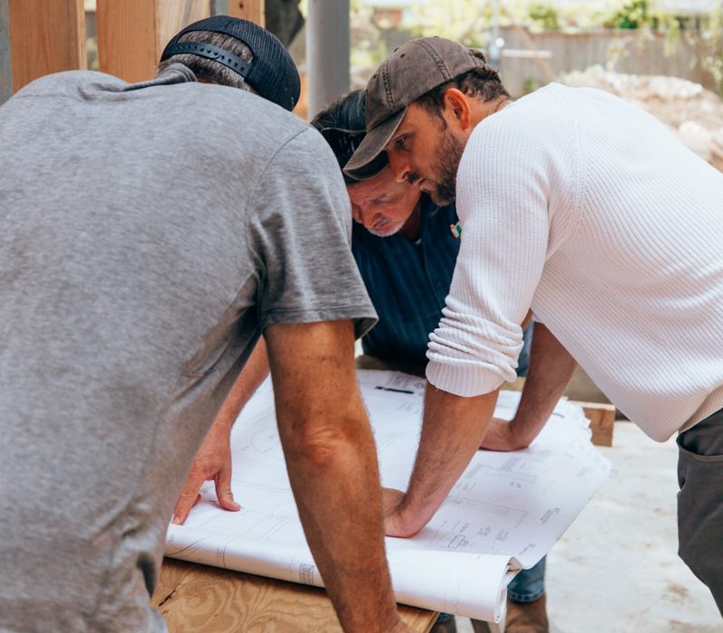 Trois artisans lisent un plan sur le chantier