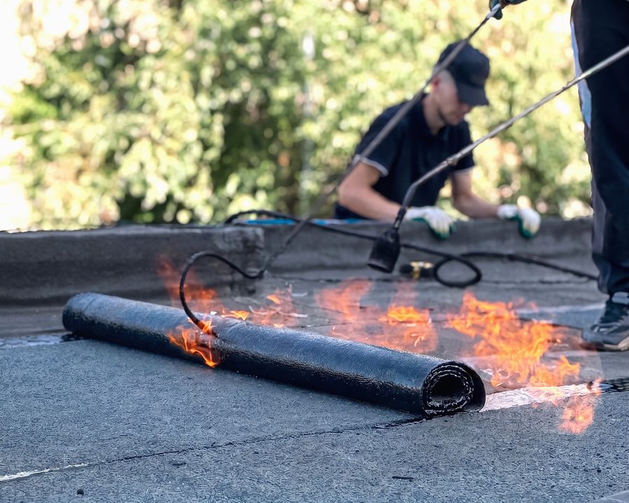 Un étancheur soude au chalumeau un rouleau de membrane bitumineuse sur un toit-terrasse